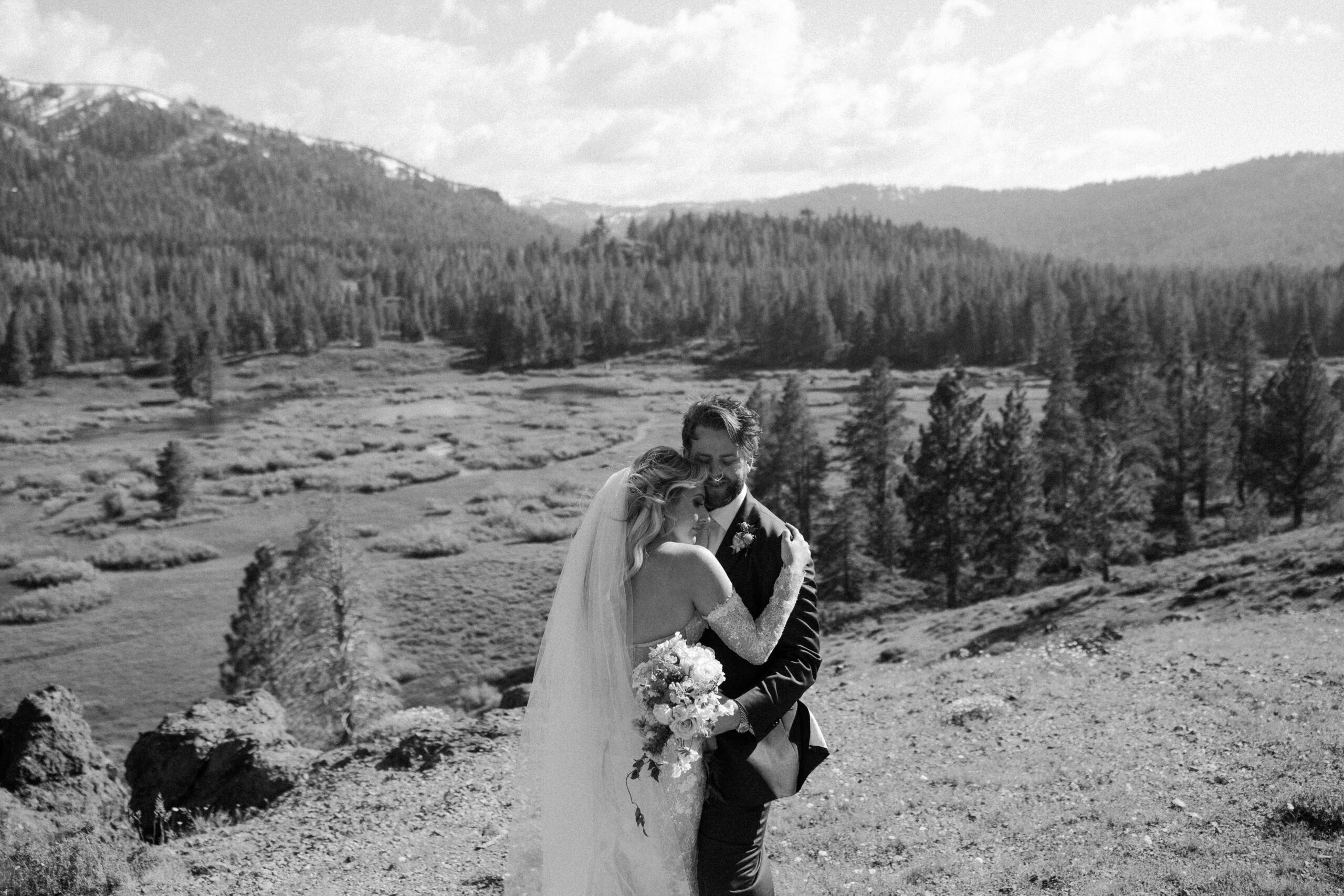 bride and groom pose with beautiful valley landscape dotted with water